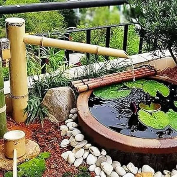 Petite fontaine japonaise solaire en bambou installée sur un balcon urbain avec galets.