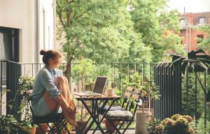 Femme profitant d’un balcon urbain verdoyant avec table pliante en bois, plantes en pot et ambiance naturelle, idéale pour travailler ou se détendre en extérieur.