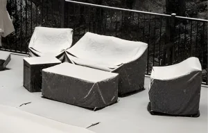 Ensemble de mobilier de jardin sur une terrasse, comprenant un canapé, deux fauteuils et deux tables, tous recouverts de housses de protection claires.