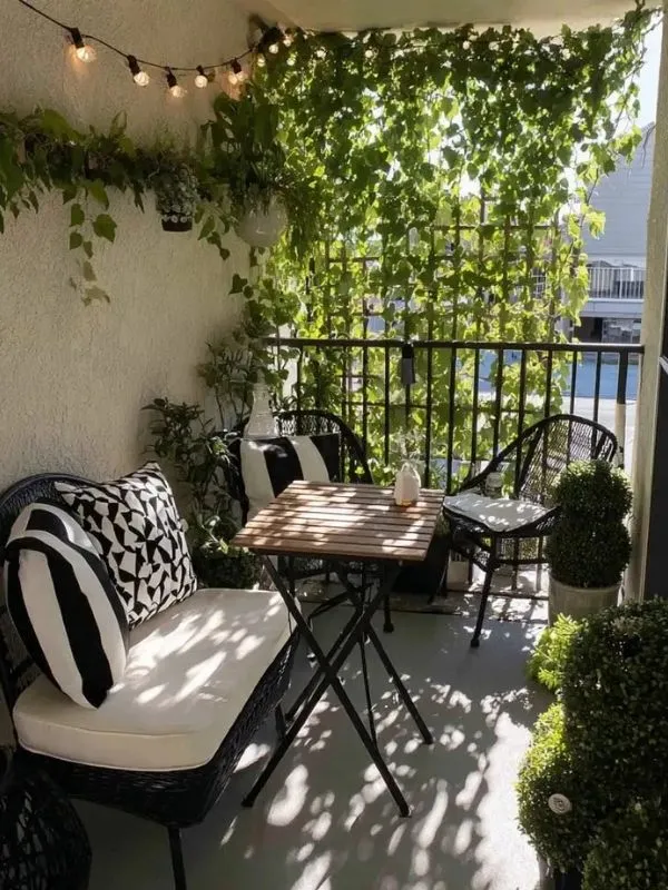 Aménagement balcon cosy avec banquette, coussins noir et blanc, table basse et mur végétal dense pour un espace zen.
