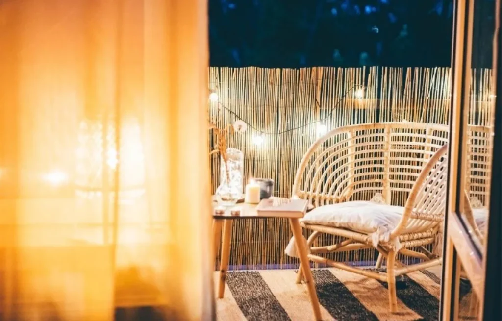 Aménagement d'un balcon cocooning avec brise-vue en canisse de bambou, fauteuil en rotin et guirlande lumineuse.