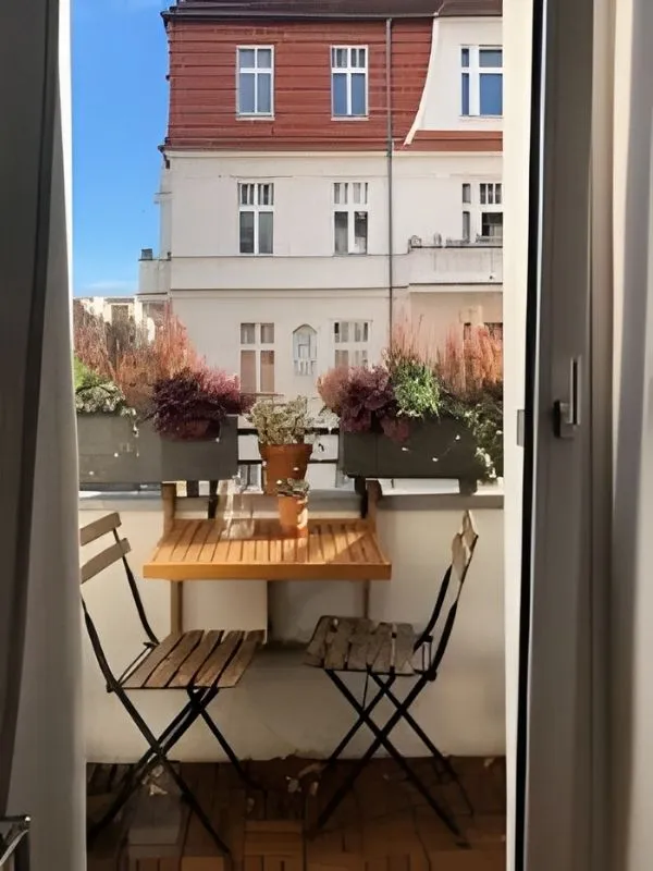 Coin repas balcon avec table pliante en bois fixée à la rambarde, jardinières de fleurs et chaises de bistro élégantes.