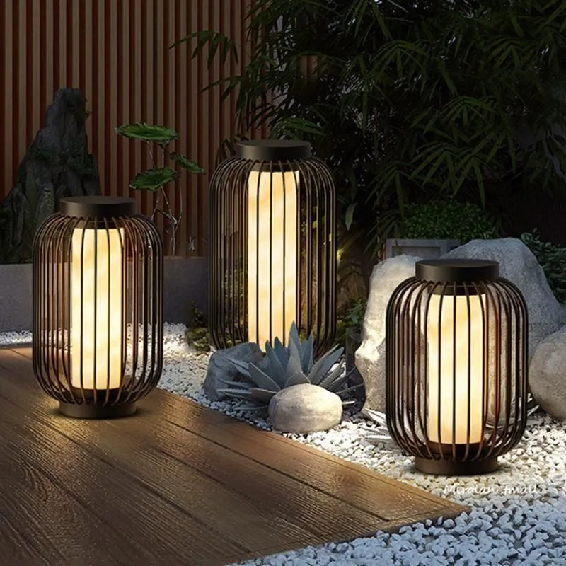 Lanterne de balcon solaire au design minimaliste noir sur sol en bois et galets blancs pour une ambiance de jardin japonais de nuit.