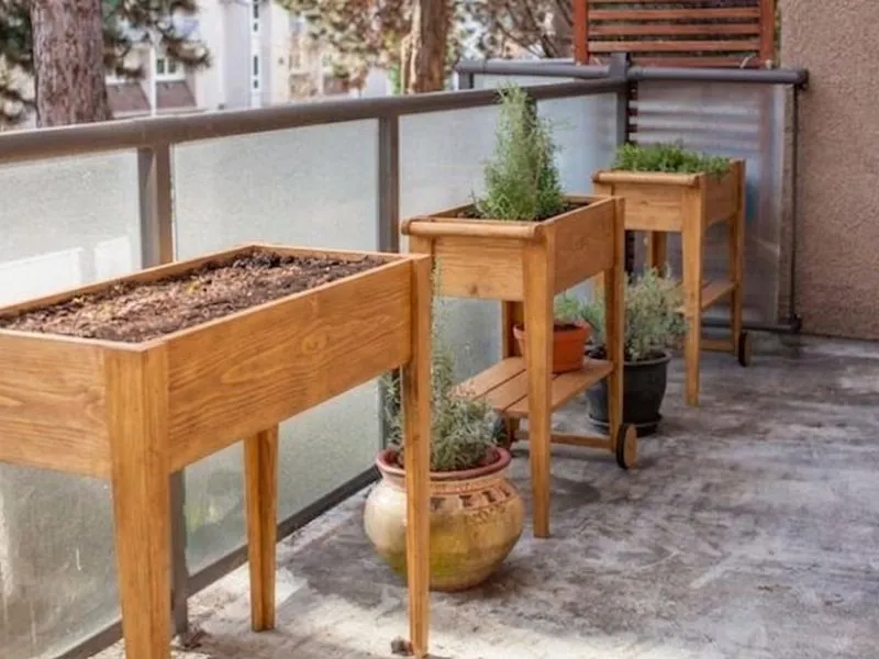 Bacs potagers sur pieds en bois installés en ligne sur un balcon d'appartement.