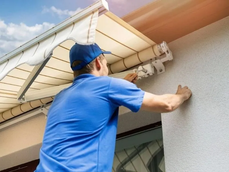 Artisan installateur fixant un store banne beige rayé sous le plafond d'un balcon