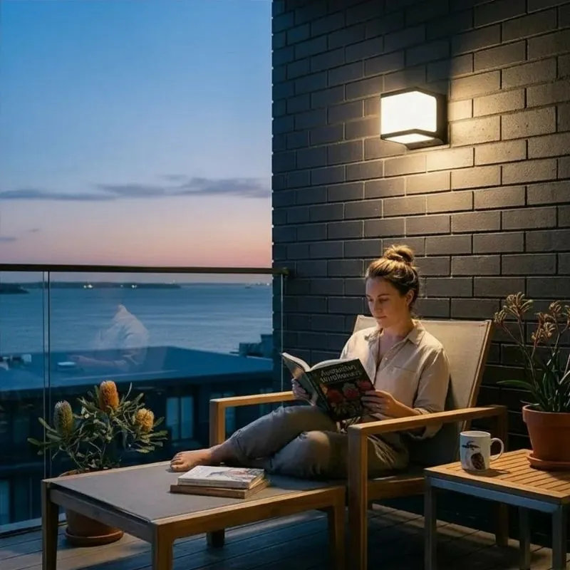 Éclairage solaire mural extérieur IP65 pour balcon, puissant avec panneau intégré, installé sur mur en brique près d'une femme lisant, vue mer et coucher de soleil.